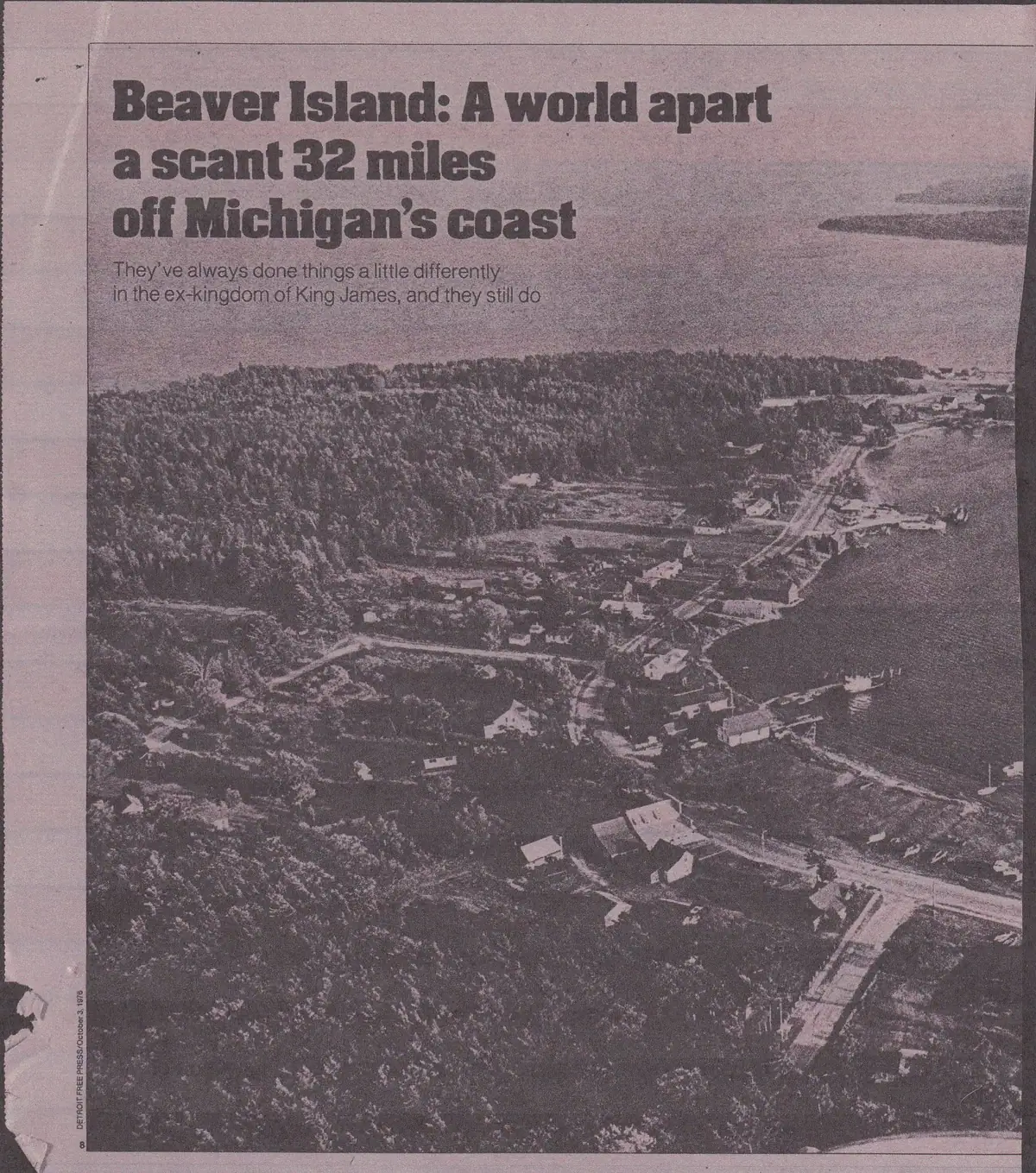 A newspaper page with an aerial photograph of a wooded settlement beside a shoreline.