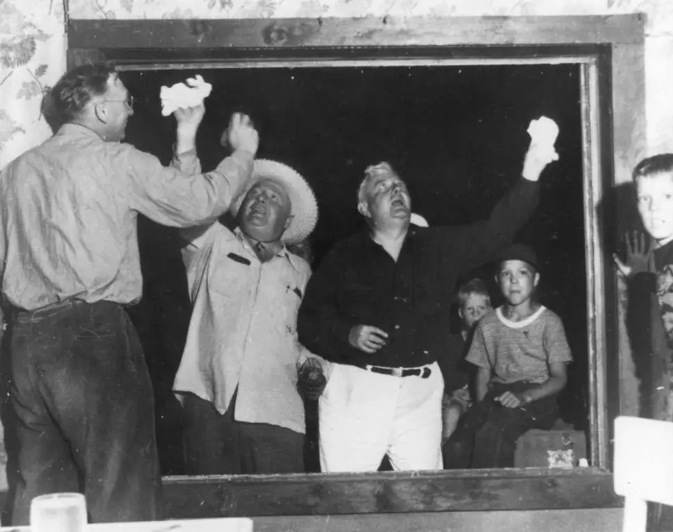 Black-and-white photograph of adults and children raising white cloths in and around a large opening.