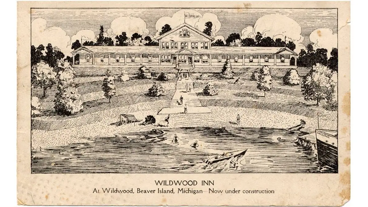 Black-and-white postcard illustration of a large inn, landscaped grounds, beach, swimmers, and boats.
