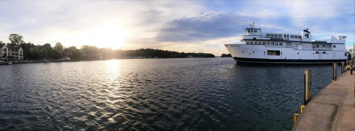 A white ferry sits beside a pier as low sunlight reflects across rippled water.