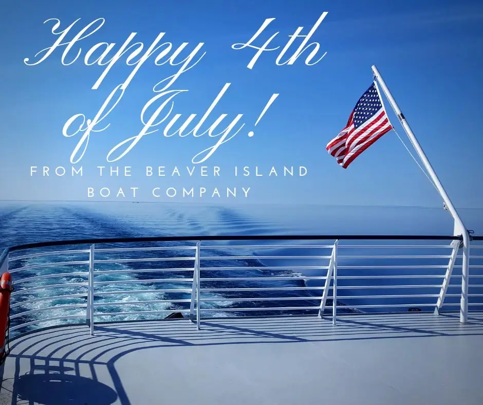 American flag flying from a passenger vessel deck above blue water and a foamy wake.
