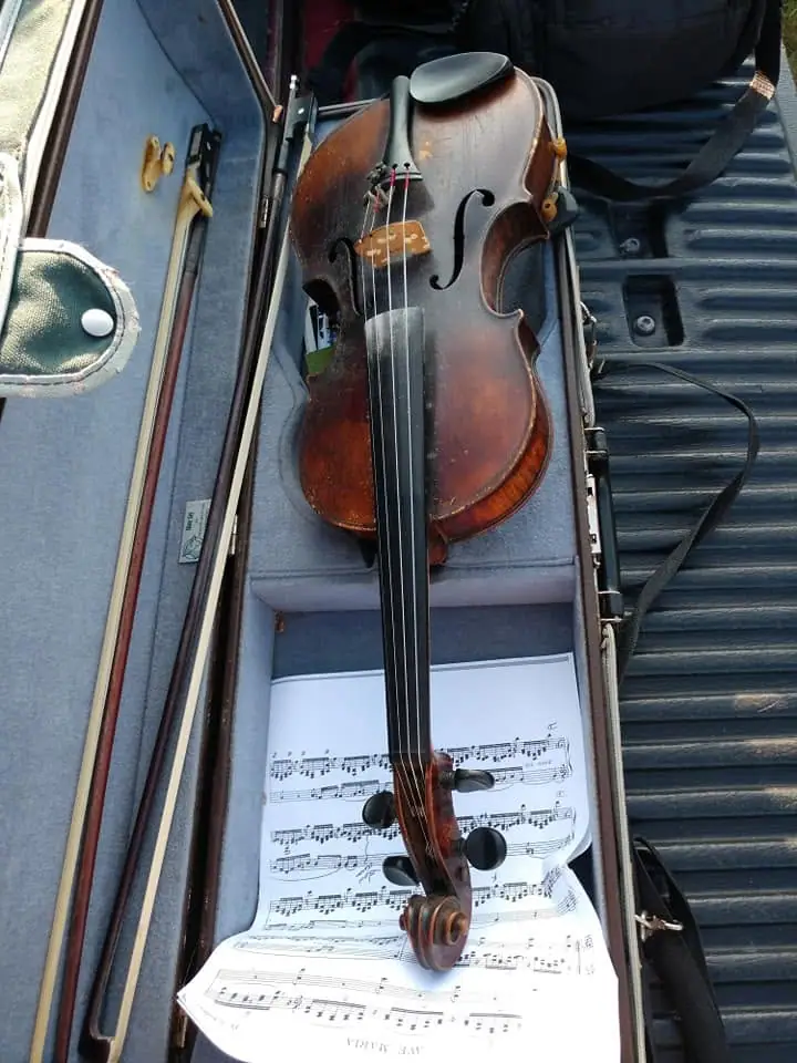 A violin, bow, and printed sheet music rest in an open instrument case.