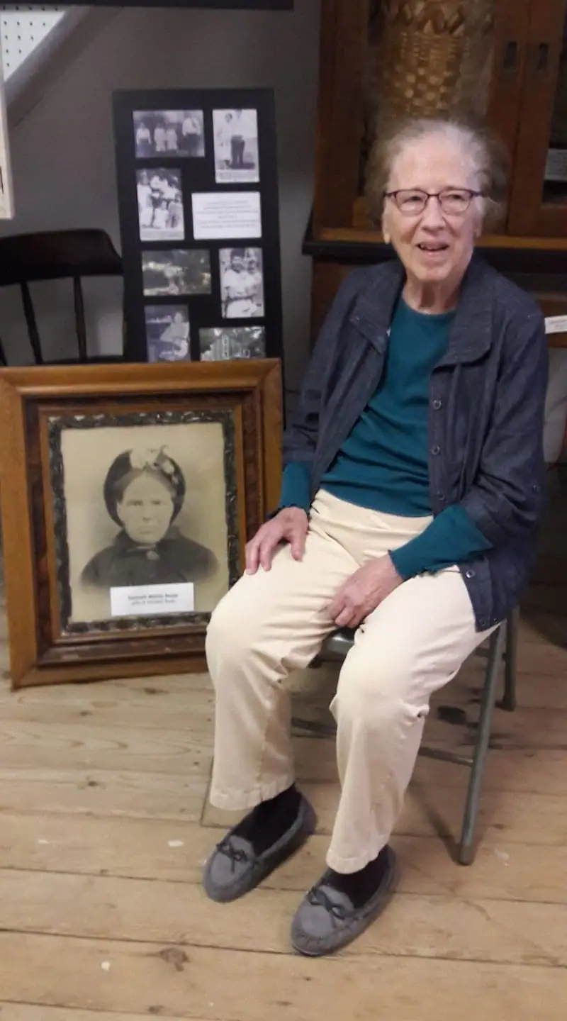 Seated woman beside a framed historical portrait and a wall display of photographs.