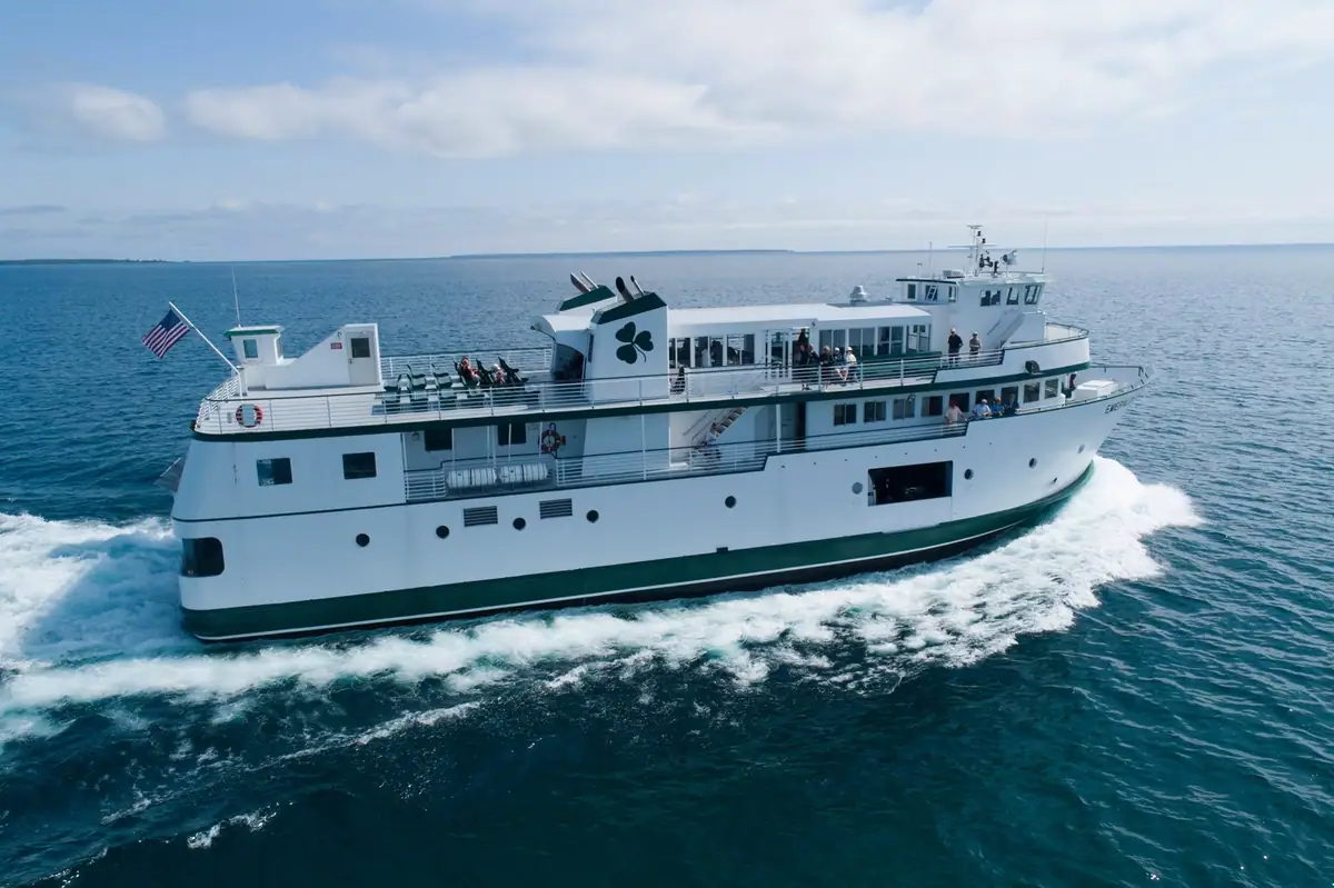 A white passenger ferry with green trim travels across open water, carrying people on its decks.