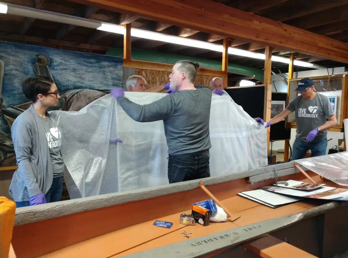 Five people in purple gloves handle large sheets of bubble wrap inside a timber-framed workshop.