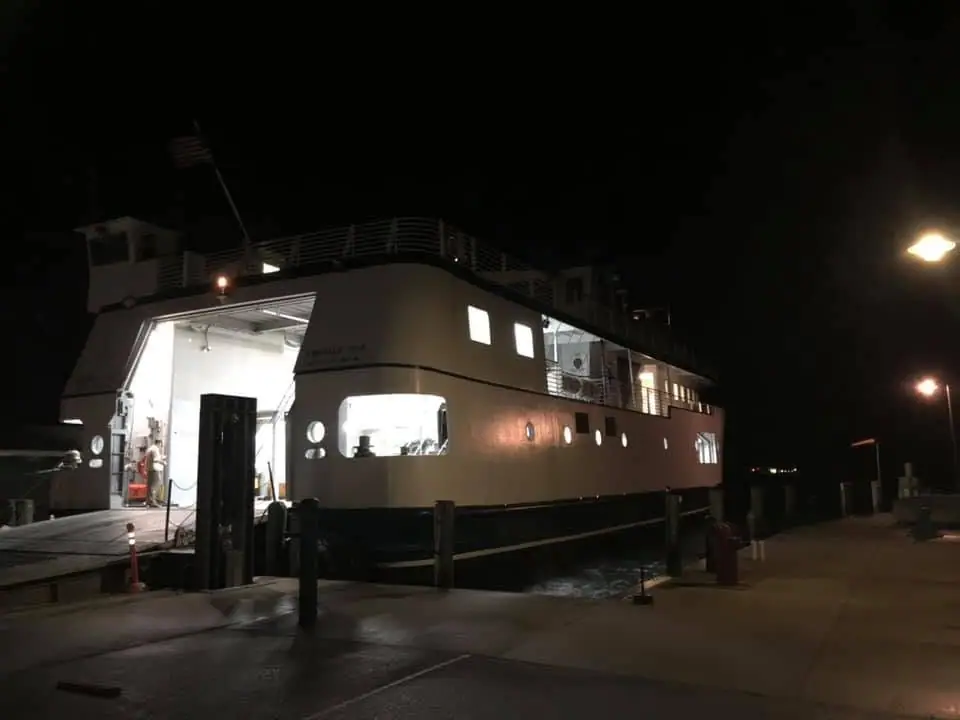A large ferry is illuminated at a dock at night, with its open vehicle bay visible.