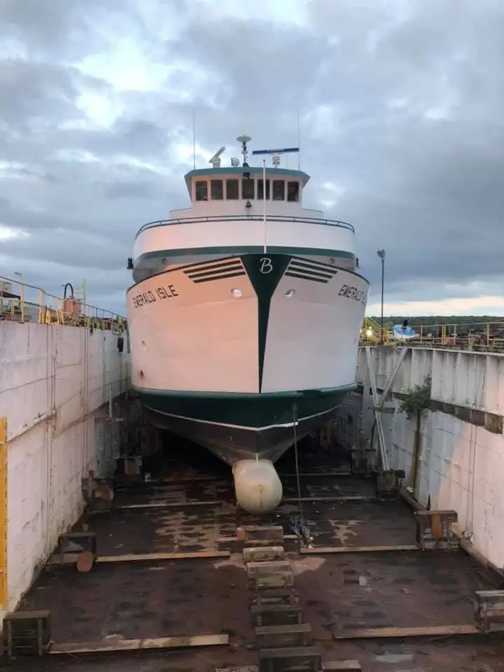 Ferry resting in a drained dry dock beneath a cloudy sky.