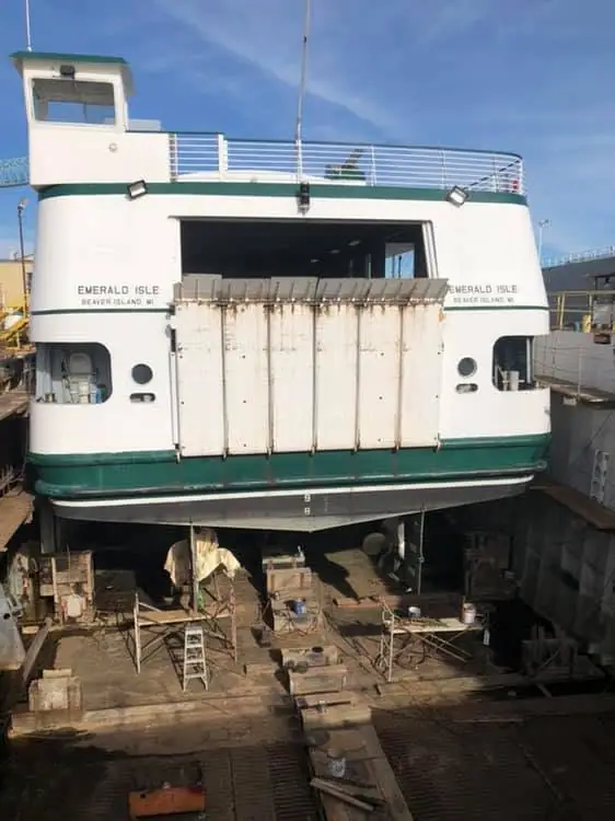 A white-and-green ferry is elevated in a dry dock with its front ramp raised for maintenance.
