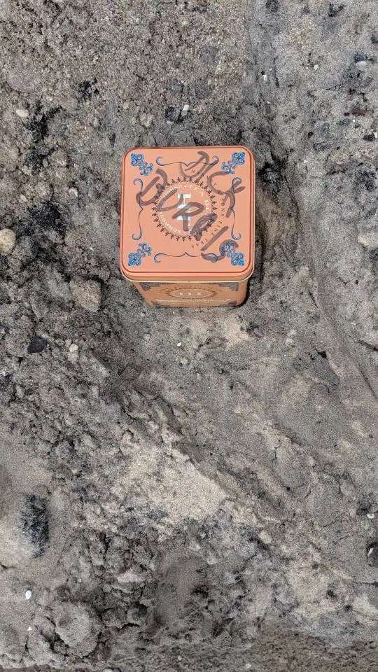 An orange decorative metal tin rests on a rough gray stone surface.