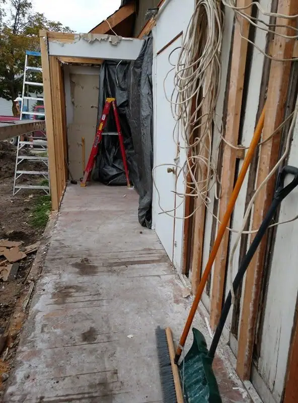 A concrete walkway beside an unfinished structure, with a ladder, coiled cable, broom, and dustpan visible.