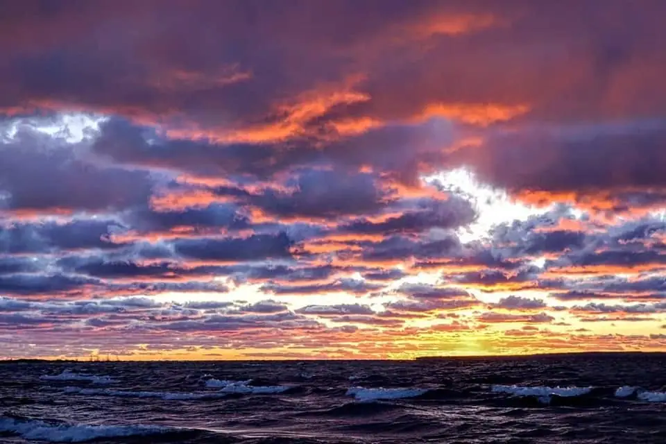 Sunset light breaks through layered clouds above dark, choppy water.