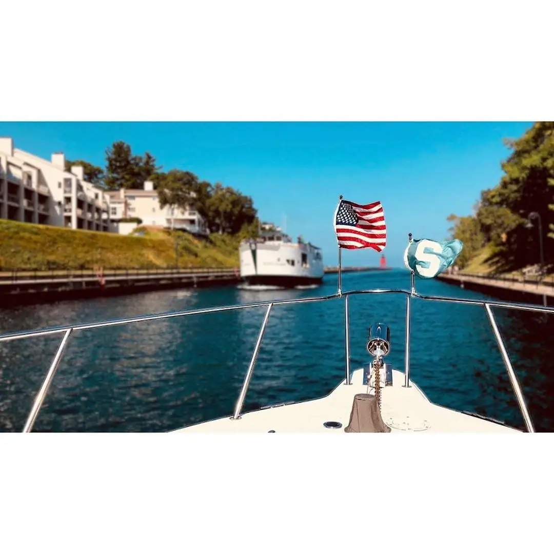 A ferry appears ahead as a boat approaches a narrow channel, with two flags flying from the bow.