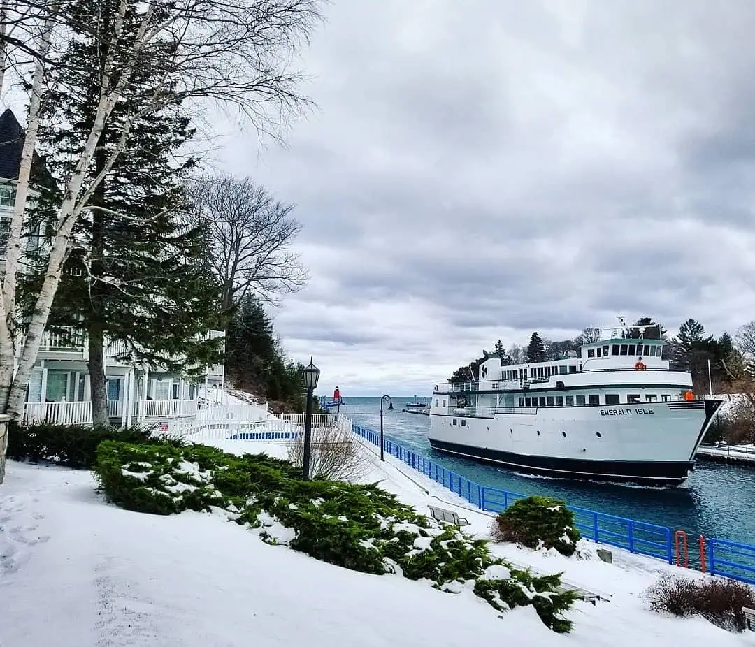 A white passenger ferry marked “EMERALD ISLE” beside a snowy waterfront under a cloudy sky.