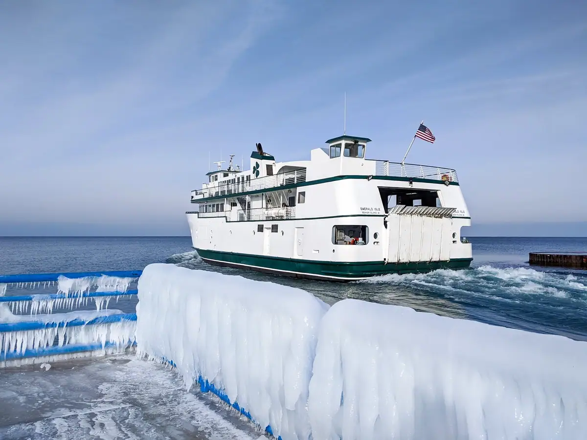 White ferry passes an ice-covered pier, with an American flag flying above its upper deck.