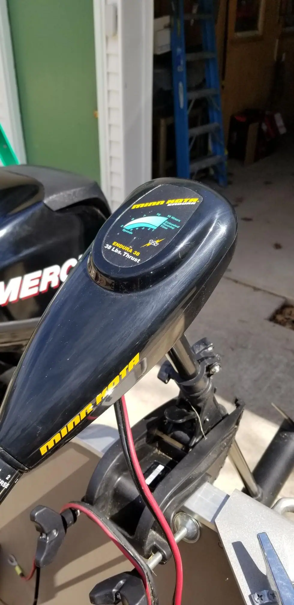 Close-up of a dark electric trolling motor mounted beside another outboard motor in a garage or workshop.
