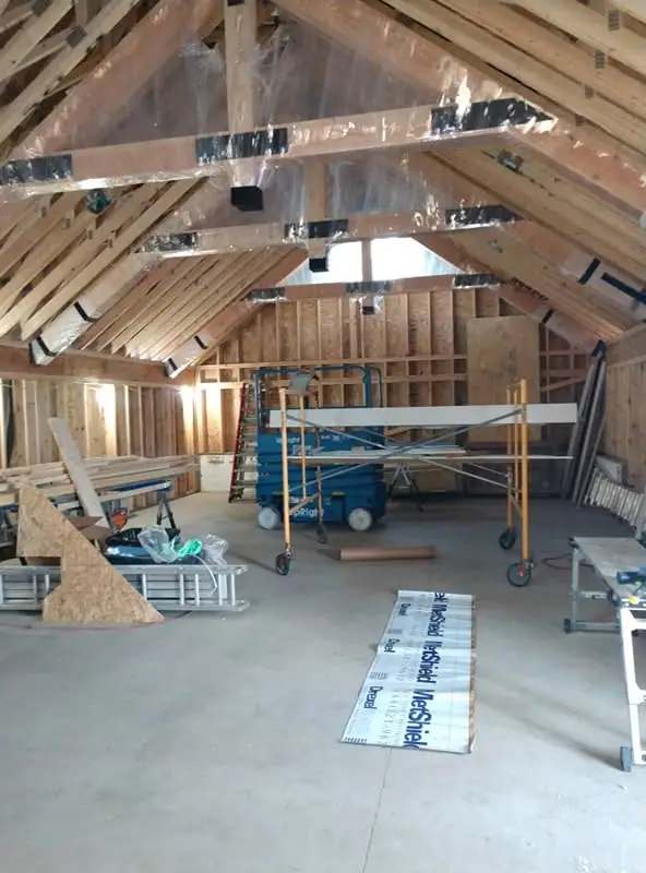 Interior construction space with exposed rafters, plastic sheathing, a blue scissor lift, and rolling scaffolding.