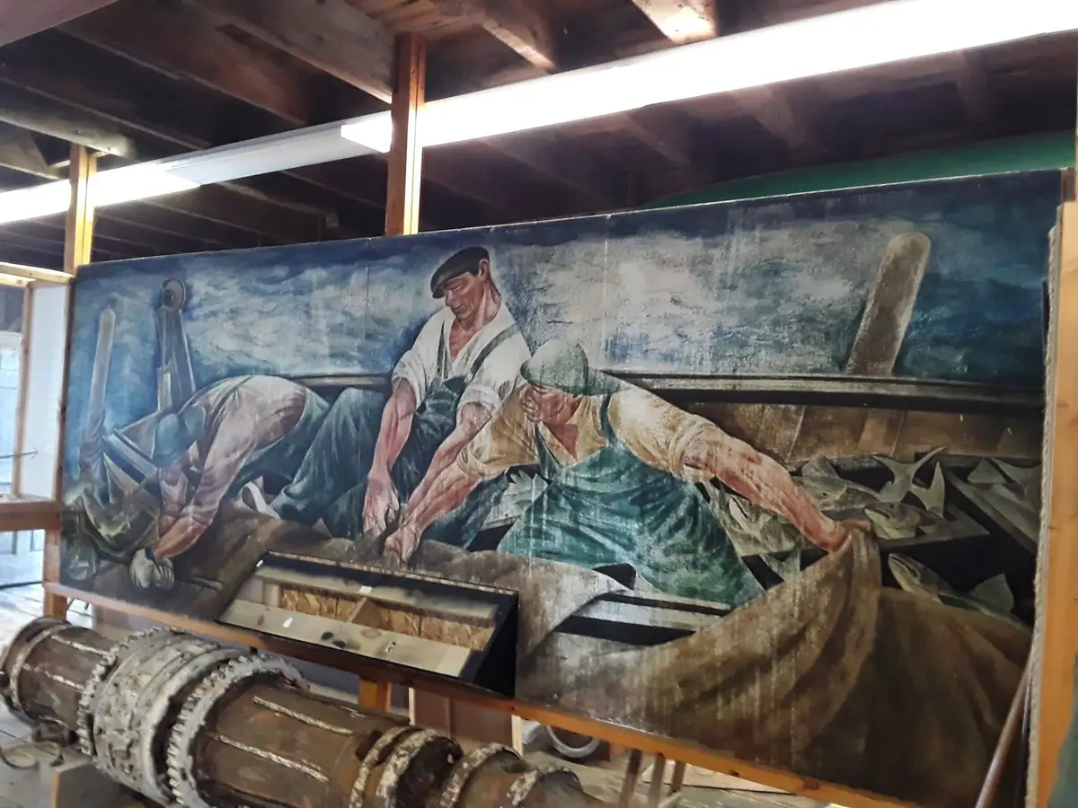 Photograph of a mural showing three men hauling fish aboard a boat indoors.