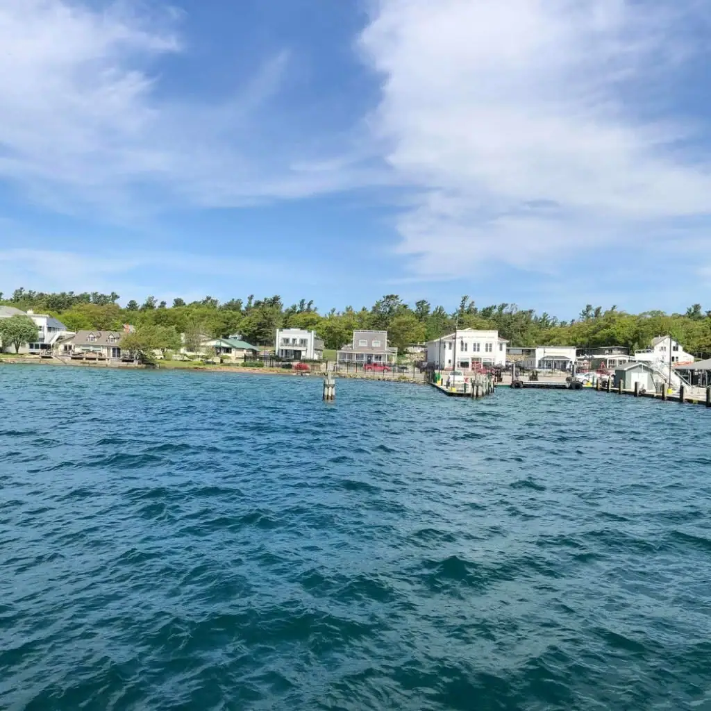 Waterfront buildings and docks line the shore beyond rippling blue water beneath a bright, cloud-filled sky.