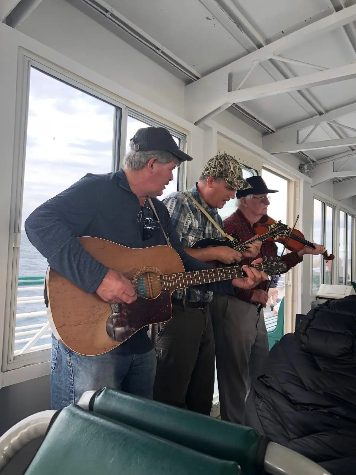 Three men play guitar, mandolin, and violin inside a passenger vessel.