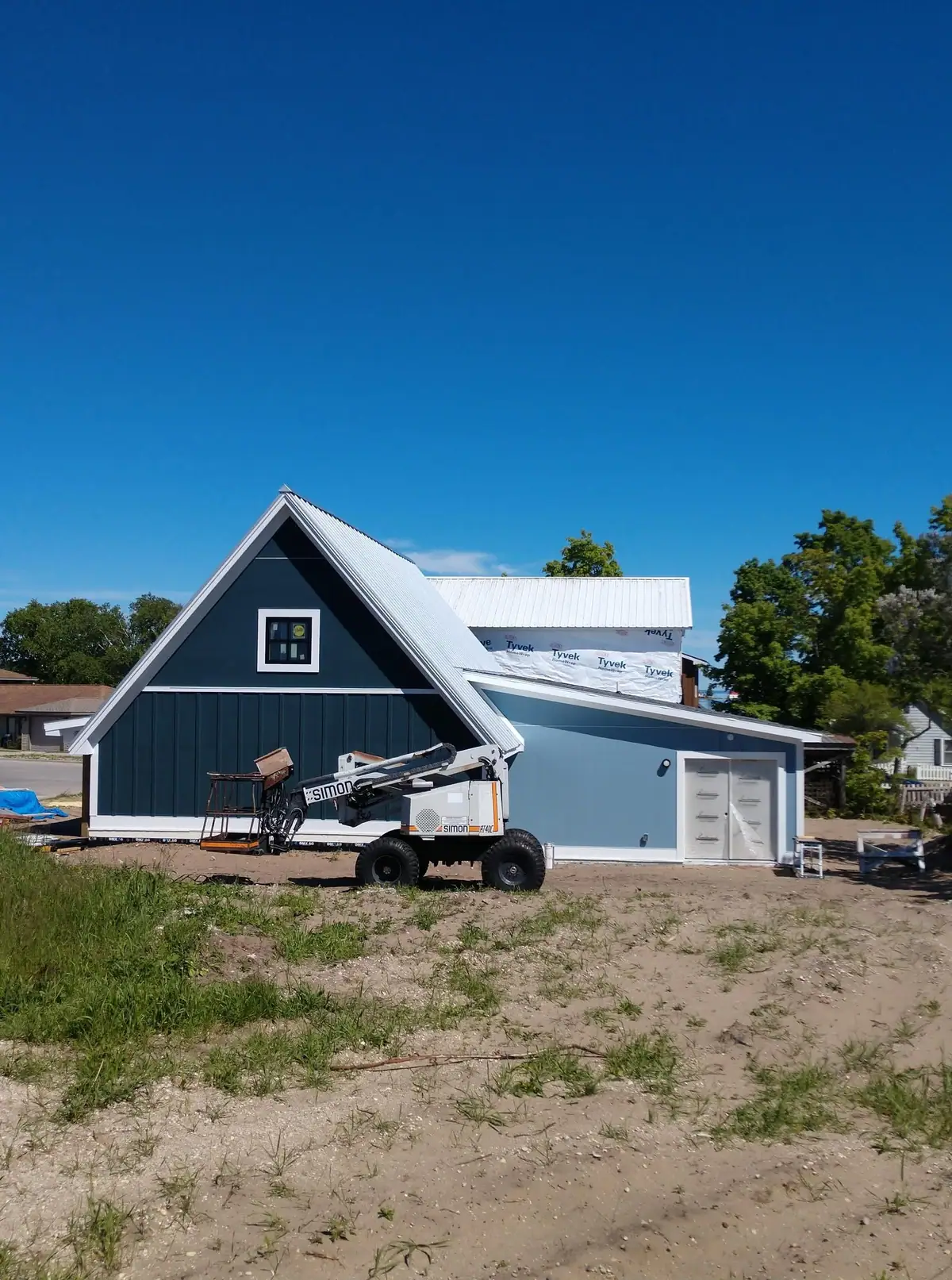 A blue gabled building under construction with a white lift parked in front.