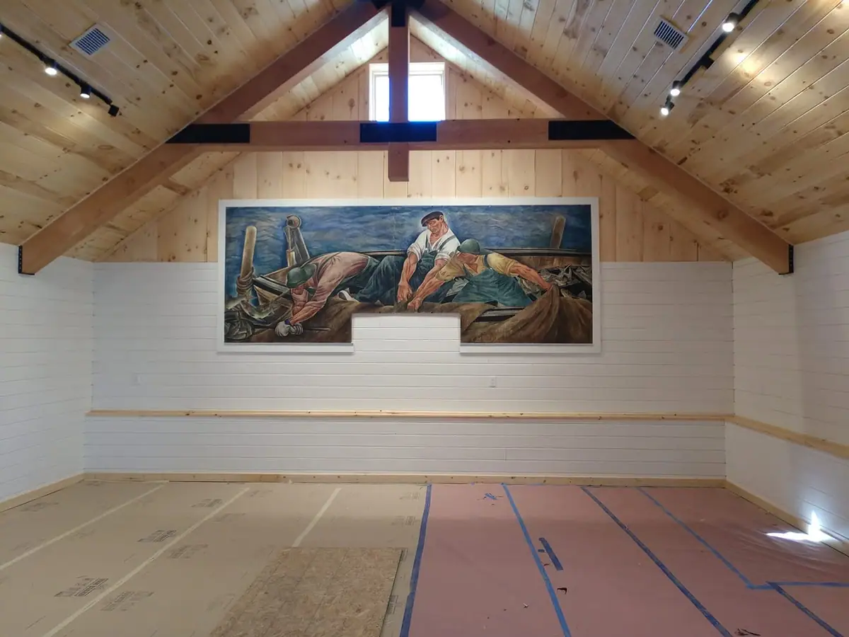 A large fishing mural hangs in a wood-paneled room with a vaulted ceiling and unfinished floor.