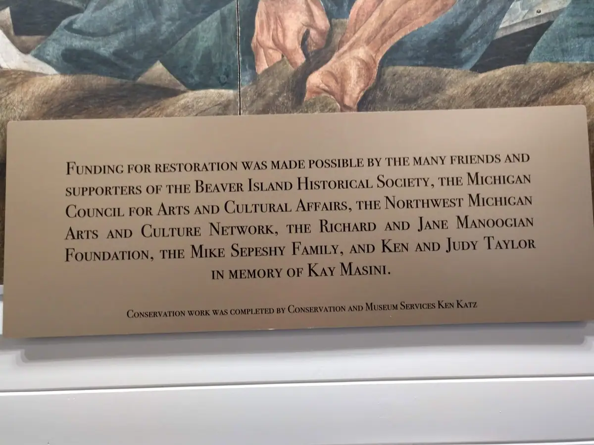 A dedication plaque beneath a partially visible painted artwork lists restoration funders and conservation credit.