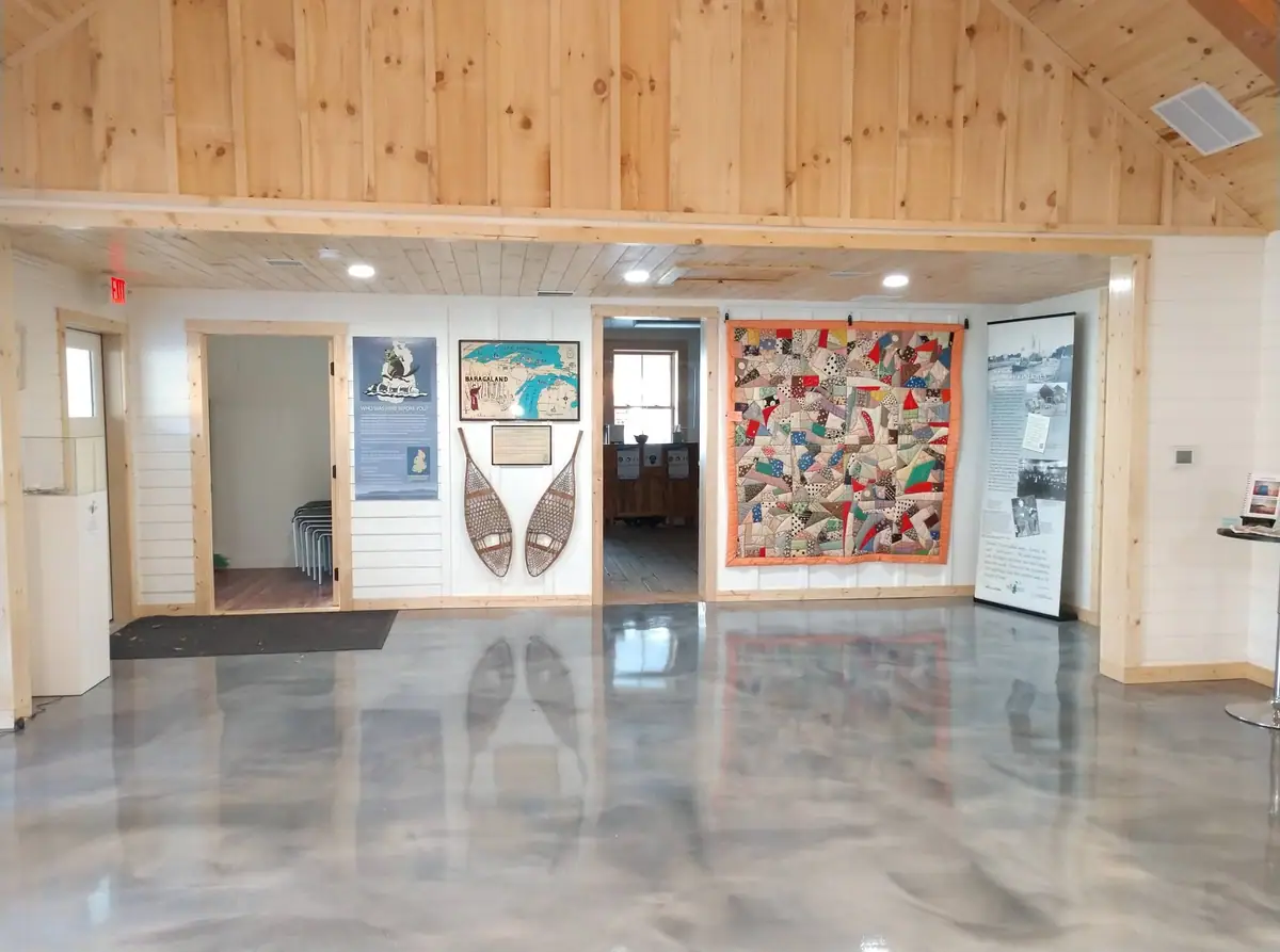 Interior exhibit space with a patchwork quilt, wooden snowshoes, display panels, and polished concrete flooring.