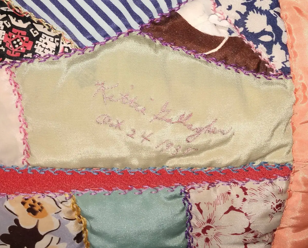 Close-up of a colorful patchwork quilt with embroidered lettering on a pale green fabric panel.