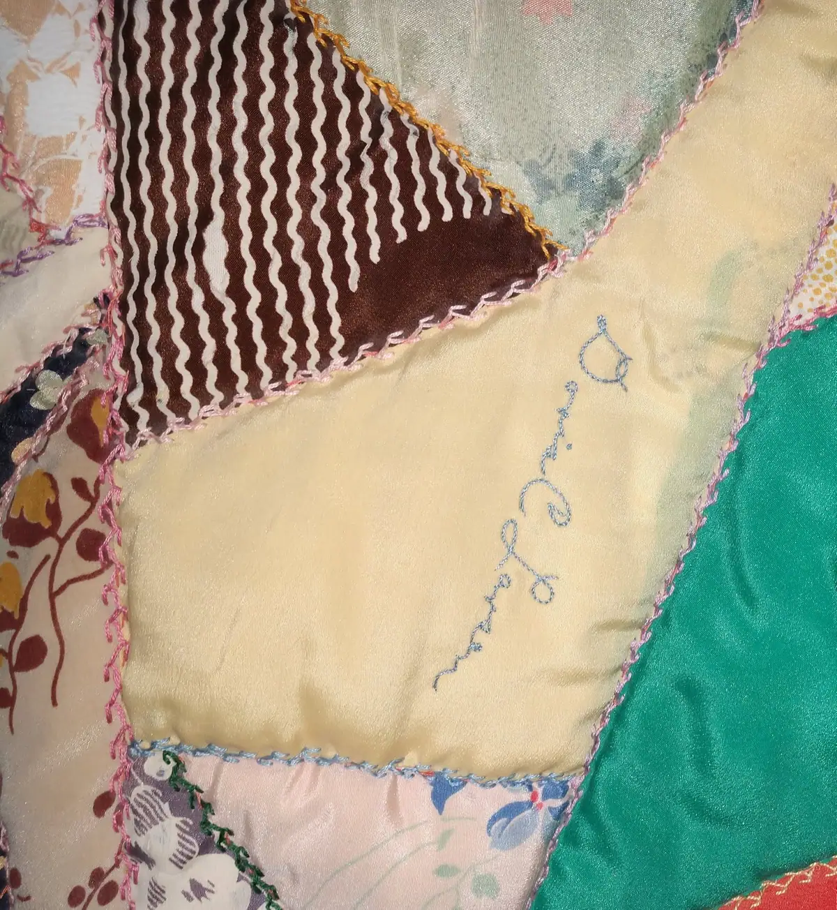 Close-up of a colorful patchwork quilt with embroidered lettering and patterned fabric pieces.