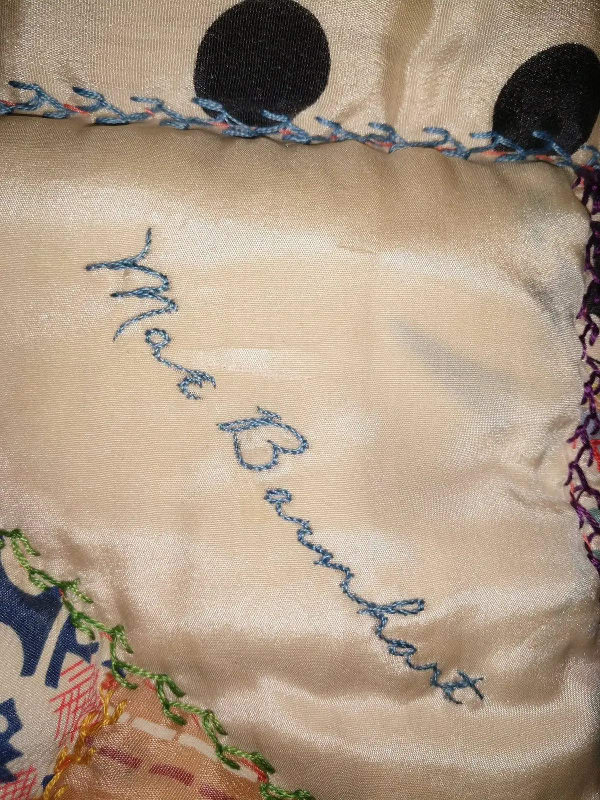 Close-up of beige fabric decorated with blue, green, red, and yellow embroidery and black circular appliqués.