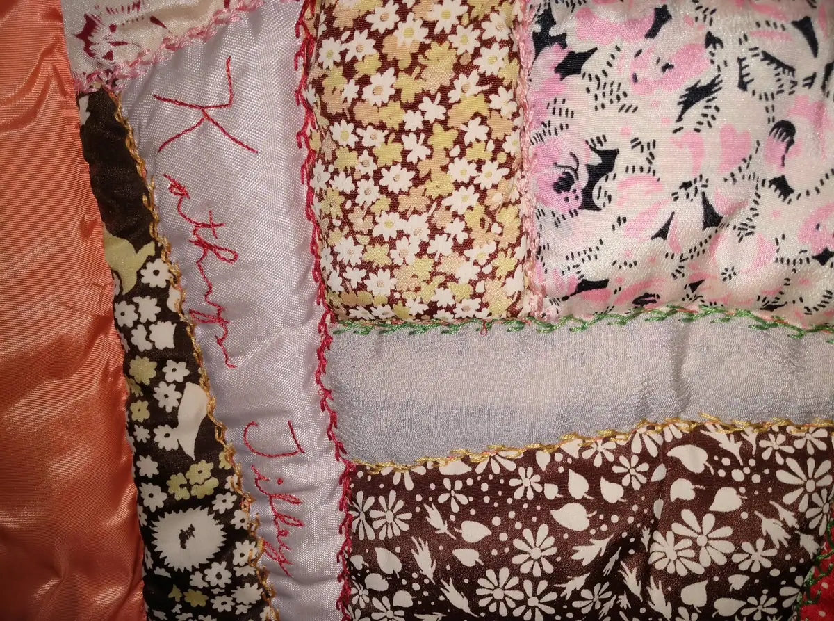 Close-up of a colorful patchwork quilt with floral fabric panels and decorative hand stitching.