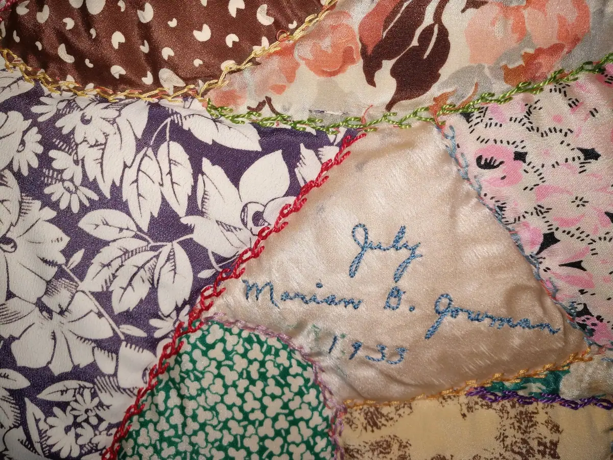 Close-up of a colorful patchwork textile with floral fabrics and a hand-embroidered name panel.