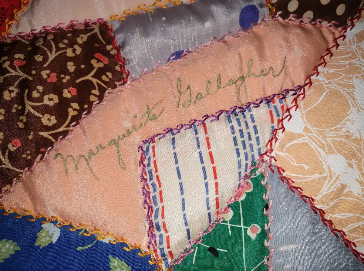 Close-up of a colorful patchwork quilt with embroidered edging and a handwritten name.