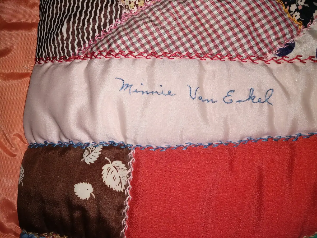 Close-up of a colorful patchwork textile with decorative stitching and a handwritten name.