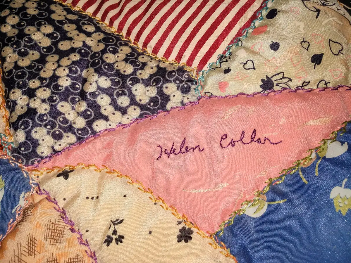 Close-up of a colorful patchwork quilt with patterned fabric pieces, decorative stitching, and a handwritten name.