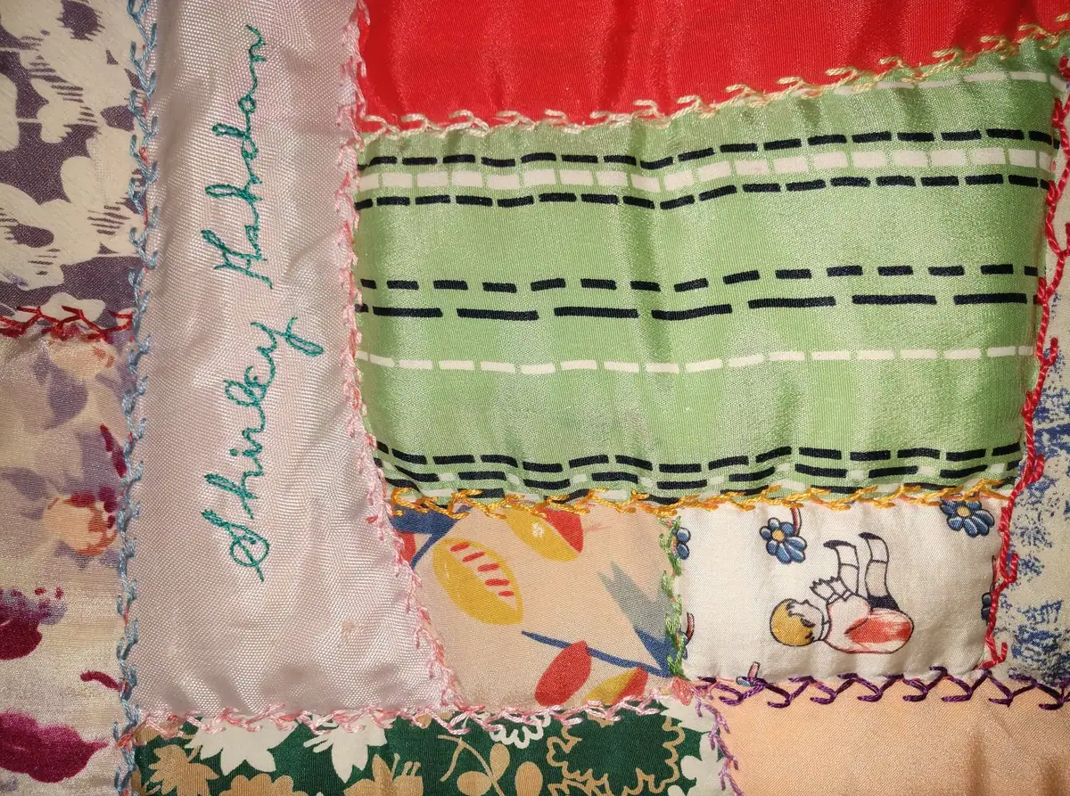 Close-up of a colorful patchwork quilt with embroidered lettering, patterned fabric squares, and decorative stitching.