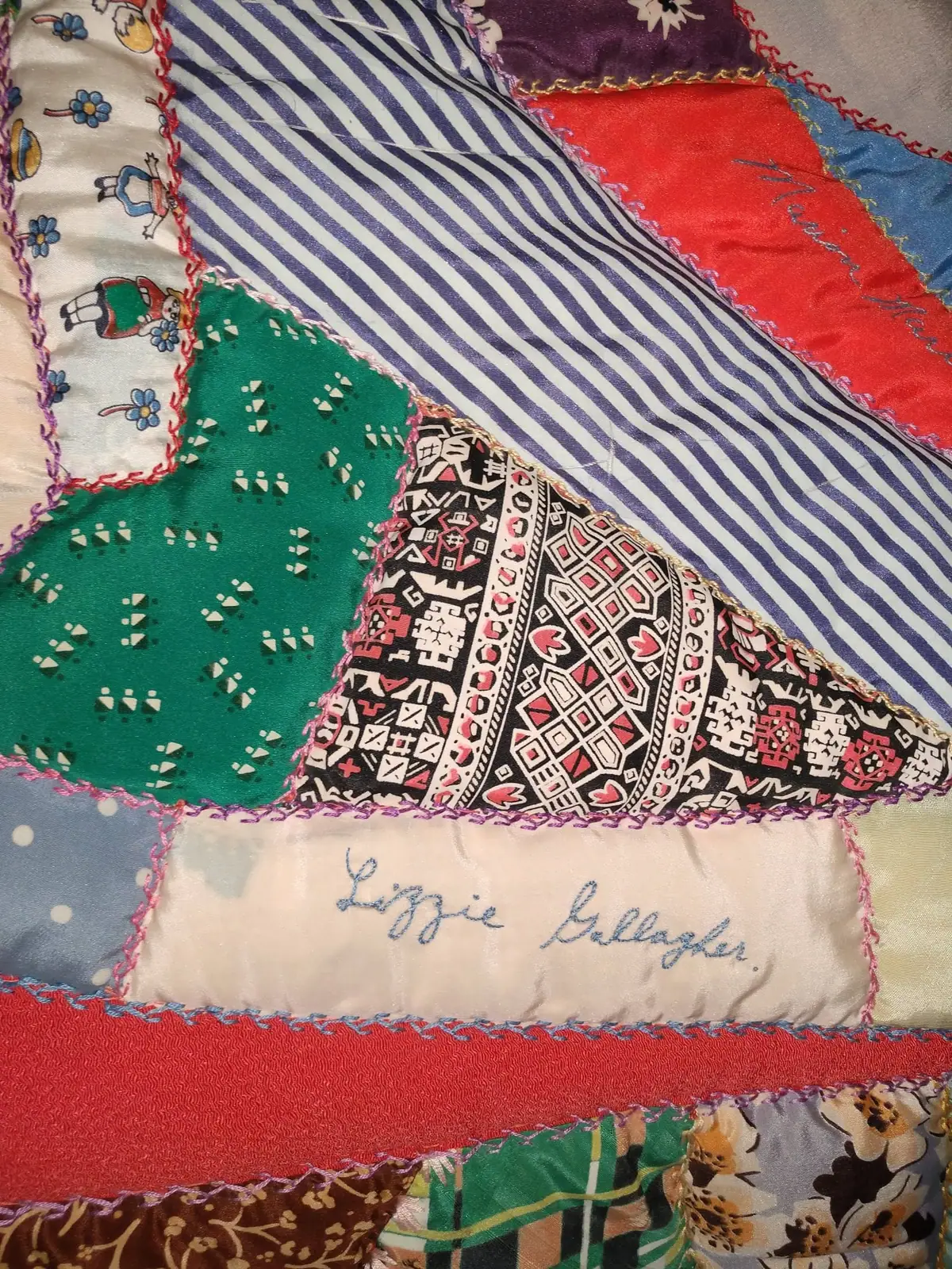 Close-up of a colorful patchwork quilt with patterned fabric pieces and an embroidered name.