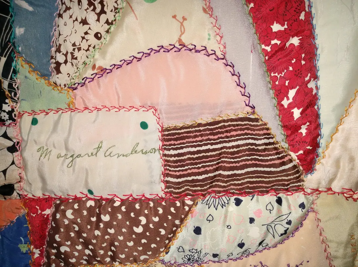 Close-up of a colorful patchwork quilt with contrasting fabrics, decorative stitching, and embroidered cursive lettering.