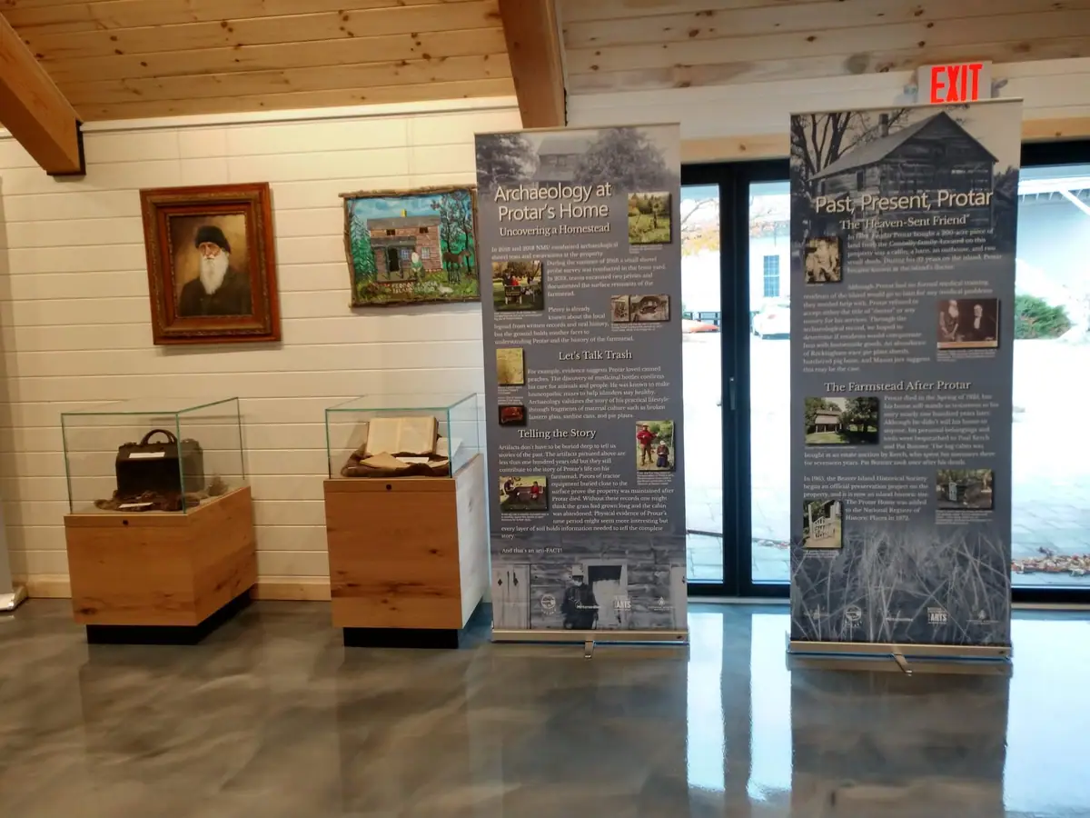 Museum exhibit interior with a framed bearded portrait, display cases, and two archaeology banners.