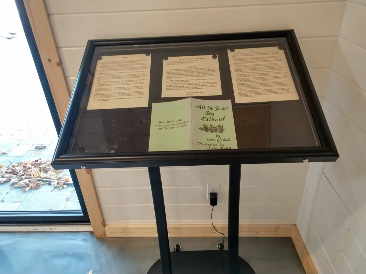 Framed display featuring an open book and printed pages in a wood-paneled interior.