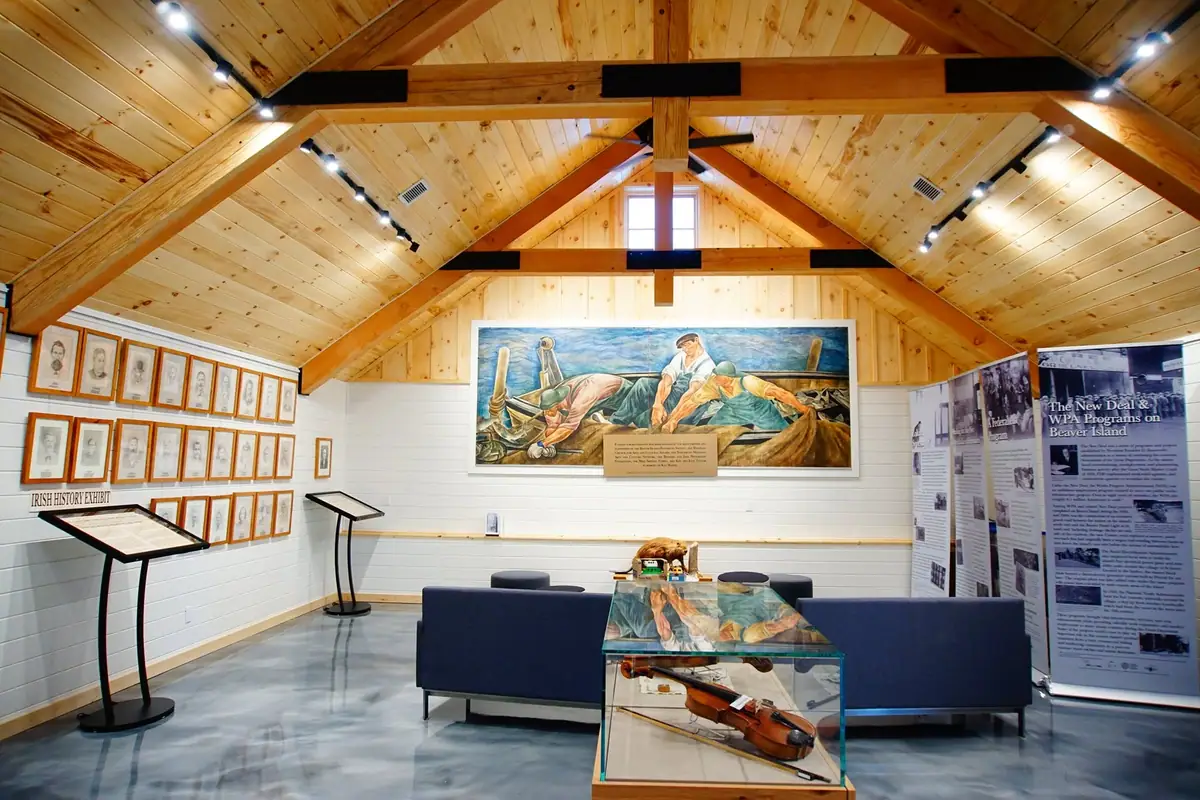 Museum interior with wooden vaulted ceiling, historical exhibits, framed portraits, a mural, and a violin display case.