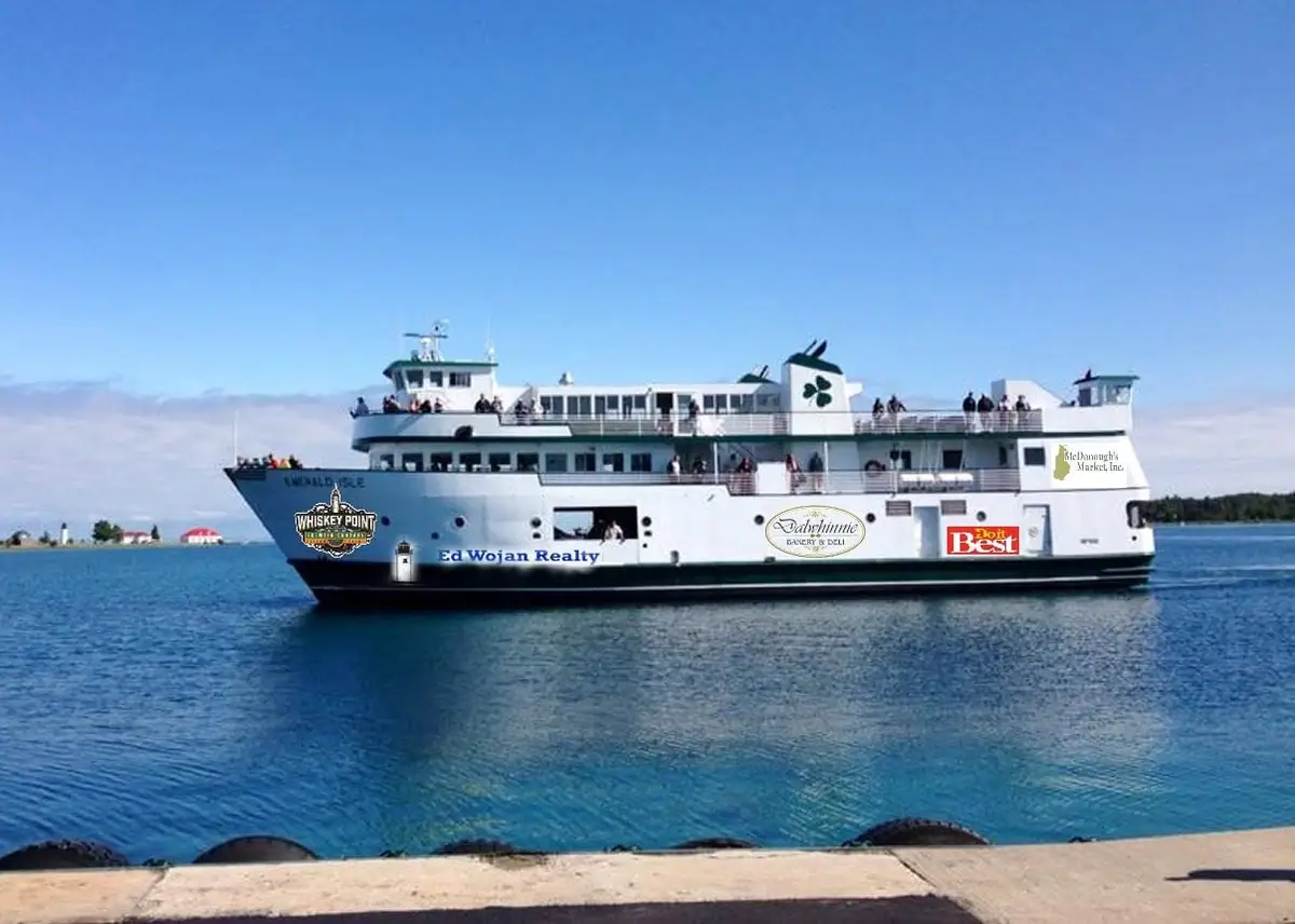 White passenger ferry with sponsor logos crosses blue water beside a concrete waterfront.
