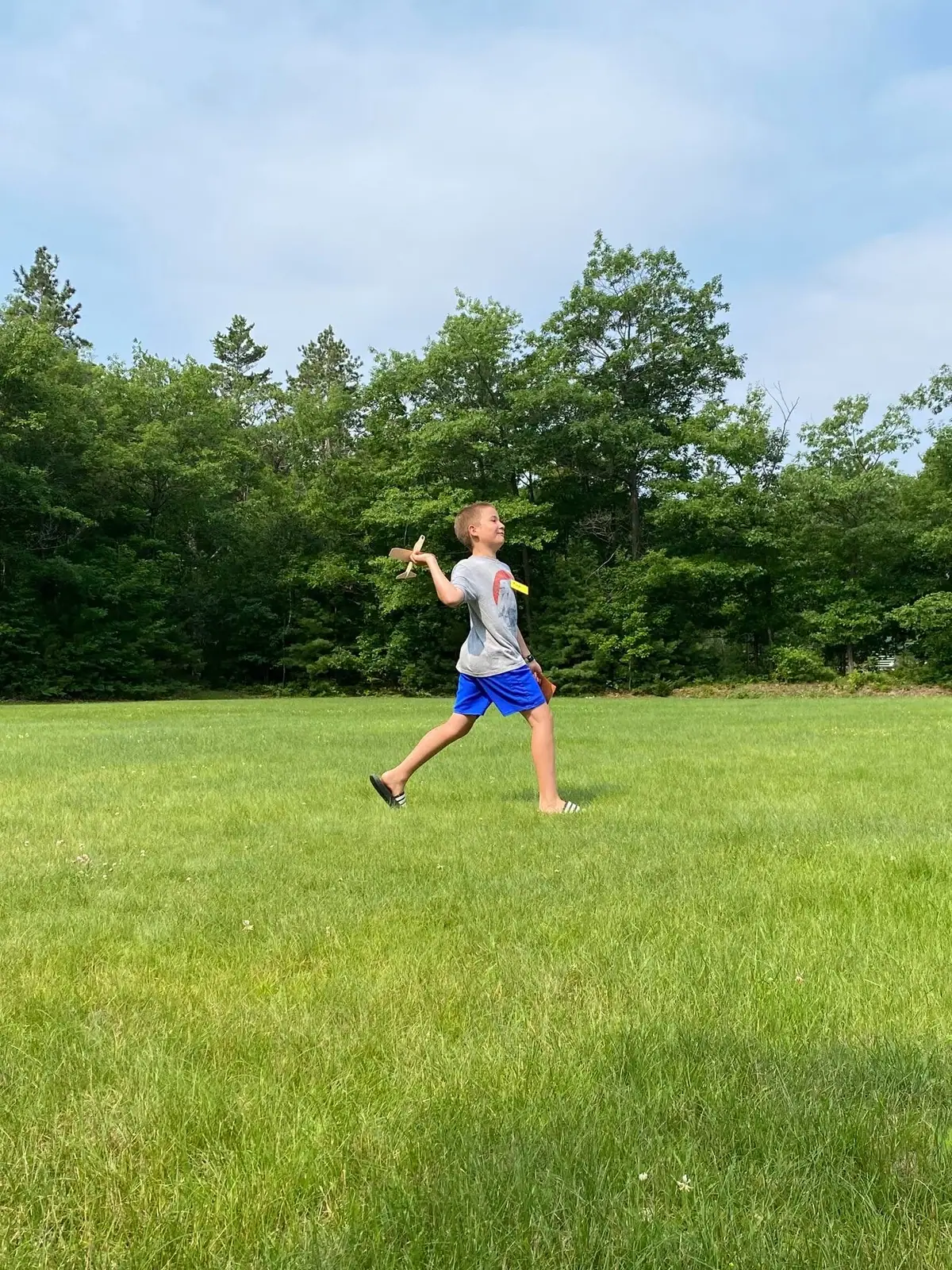 A child walks across a grassy field holding a small wooden airplane.