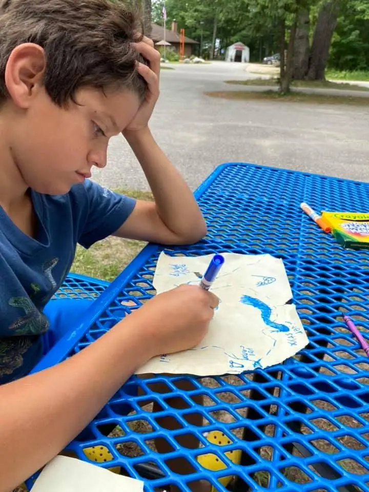 A child draws with a blue marker at a bright blue metal picnic table outdoors.