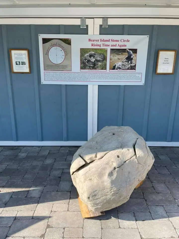 A large pale boulder stands beneath an interpretive display panel with photographs, a diagram, and printed notices.
