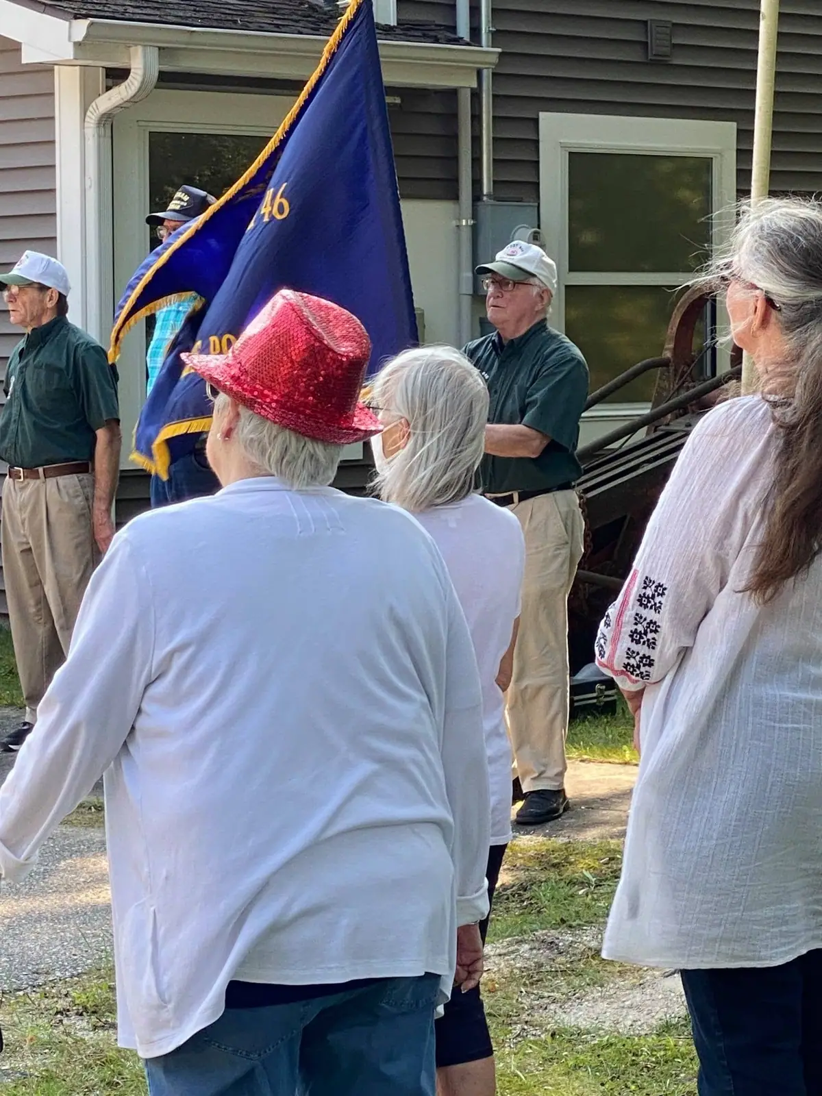 Adults gather outside a house beside a large blue flag marked with the number 46.