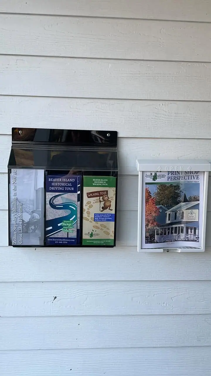 Brochures and a magazine are displayed in wall-mounted holders on white siding.