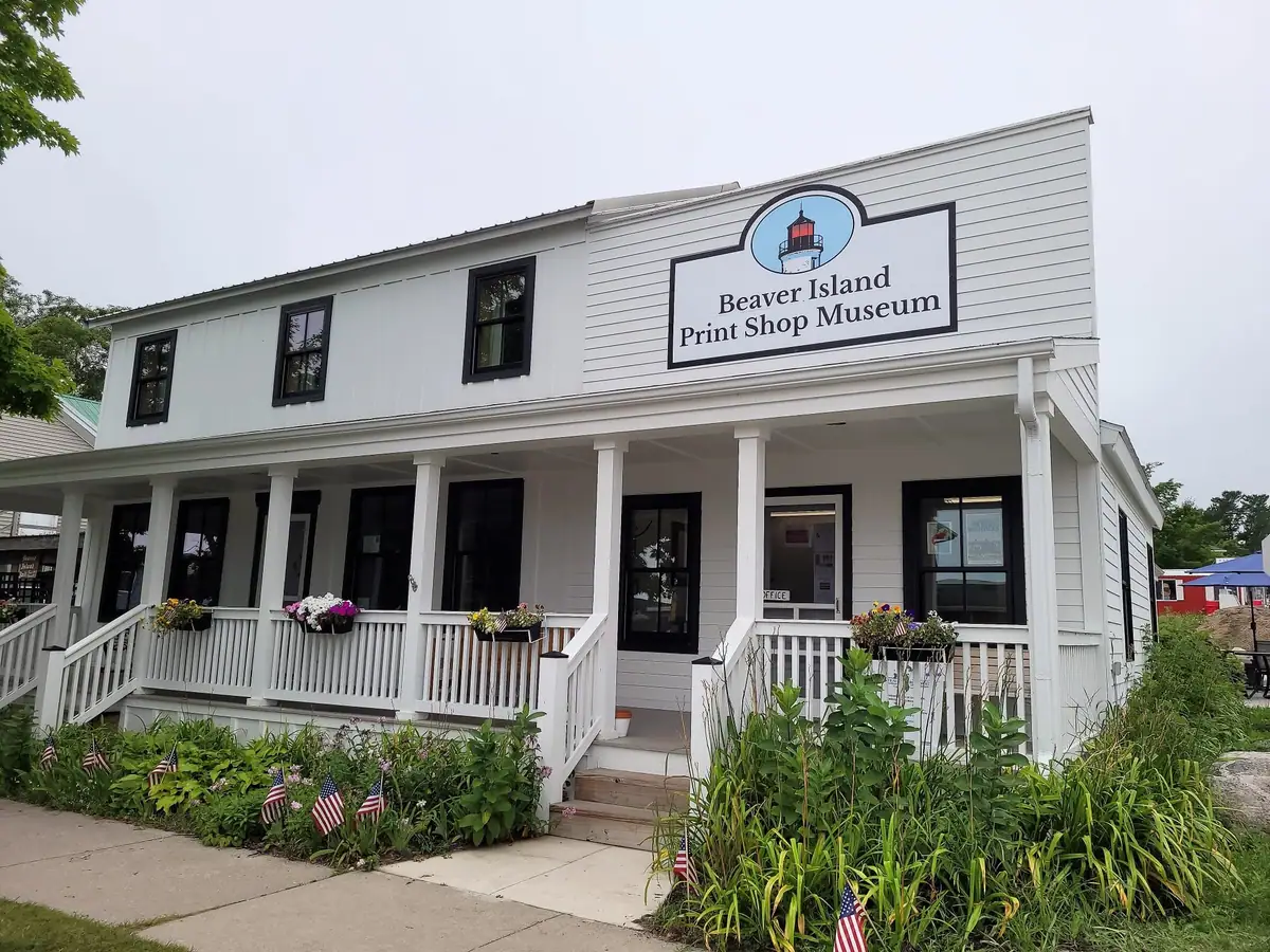 White two-story building with a covered porch, flower boxes, small flags, and a large museum sign.