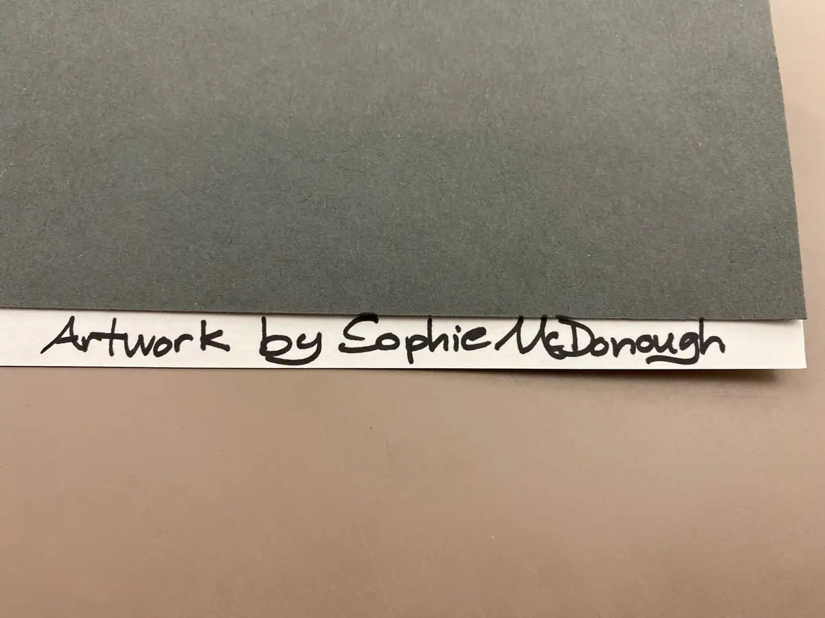 Photograph of a gray artwork with a handwritten attribution strip beneath it.