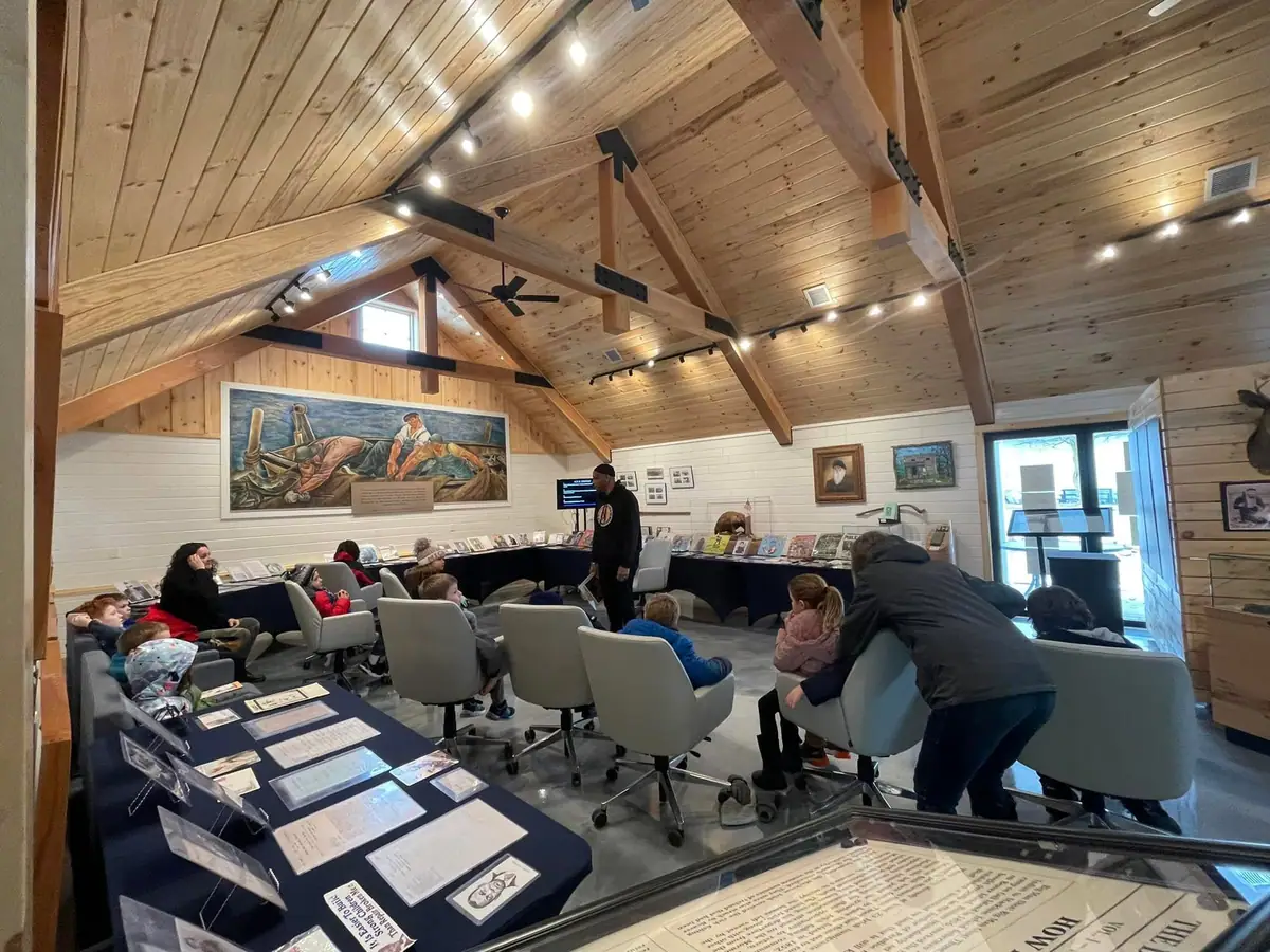 People sit among exhibit displays in a wood-paneled interior while another person stands nearby.